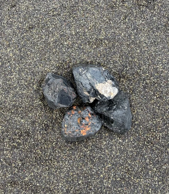 Tourmaline noire brute posée sur le sable noir, pierre de protection pour la maison